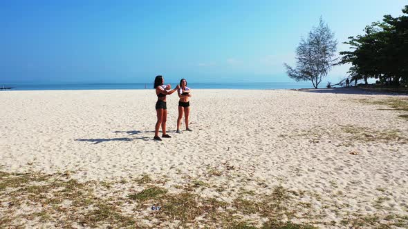 Young smiling ladies on vacation having fun at the beach on clean white sand and blue 4K background