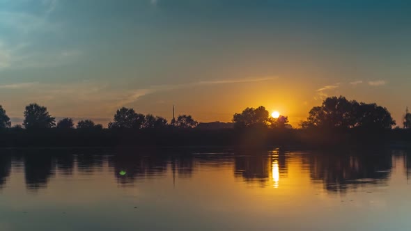 Sunset over the river. Trees and clouds are reflected in the water