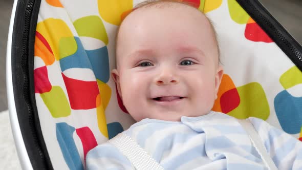 Portrait of Cute Smiling Baby Boy Sitting in Colorful Baby Seat