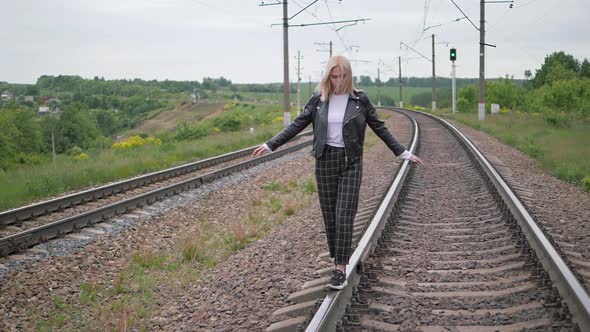 Young Woman Walks on the Rail of the Railway Tracks