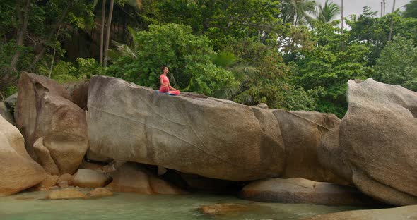 Woman Meditating on the Rock Against Tropical Forest By the Sea She is on Morning Yoga Exercise