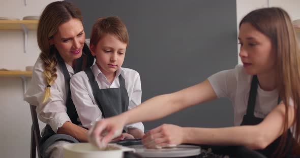 Master Teaching Mother with Her Kid to Make Clay Pot in Pottery Workshop