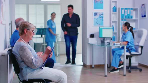 Senior Patient Signing Documents in Hospital Waiting Area