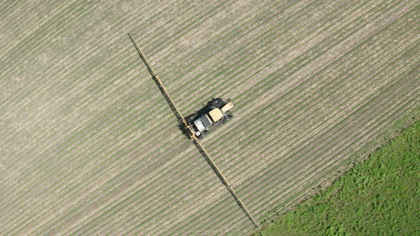 Aerial top down, farm tractor spraying pesticide, herbicide and insecticide on agricultural farm fie