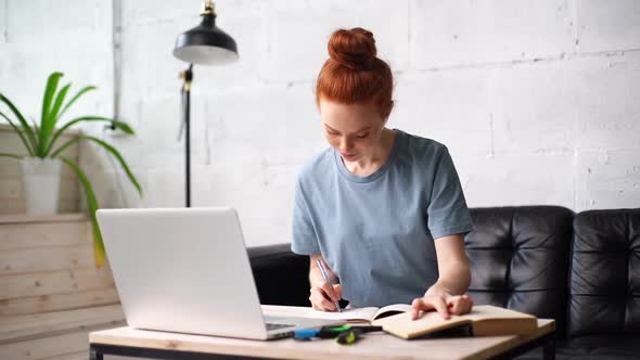 Beautiful Redhead Young Woman Student Is Noting Into the Workbook Important Information From Book.