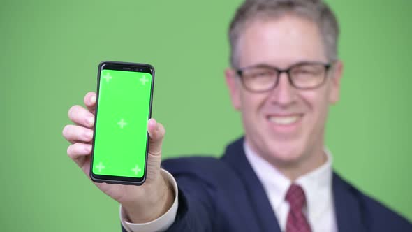 Studio Shot of Happy Mature Businessman Showing Phone