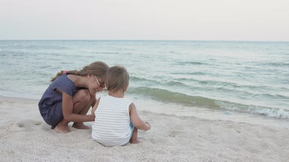 Girl Helping Her Little Brother to Look for Seashells in the Sand on the Coast