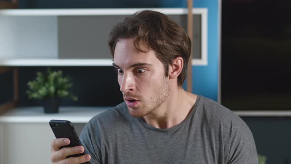 Man Is Shocked Terrible Message on His Smartphone at Home Apartment Background. Unpleasantly