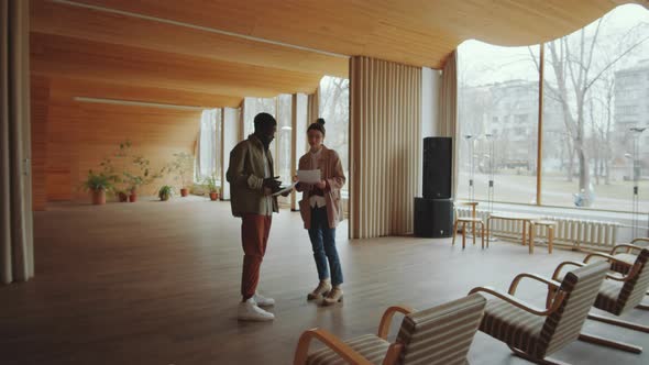 Diverse Man and Woman Discussing Documents in Modern Auditorium