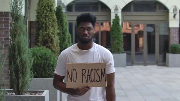 Poster NO RACISM in the Hands of a Black Guy. An African American Man in a White T Shirt Stands in