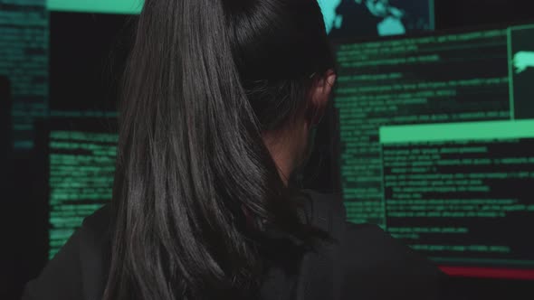 Back View Of  Asian Young Girl Hacker Hacking With Multiple Computer Screens In Dark Room