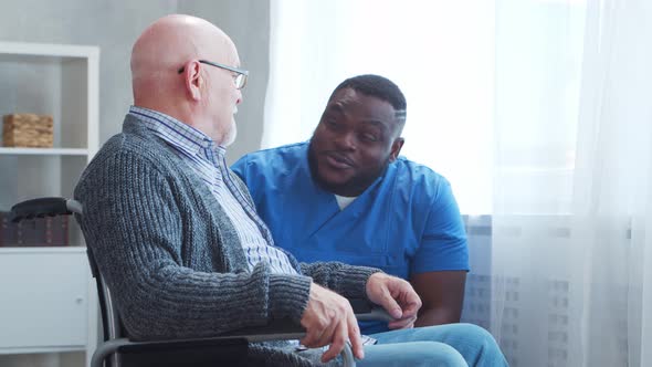 African-American caregiver and old disabled man in a wheelchair. Nurse and handicapped patient.