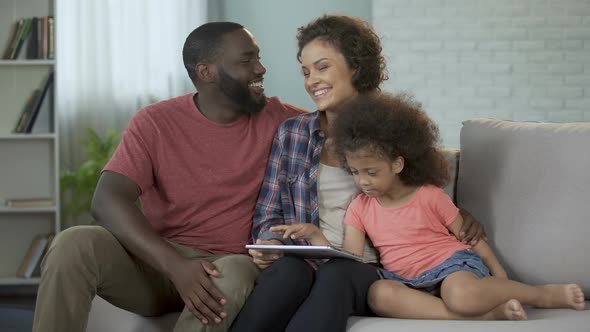 Parents showing daughter her first photos on tablet, cozy family atmosphere