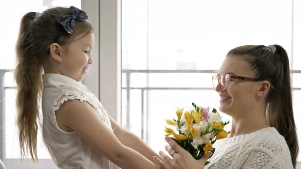 6-7 Year Old Girl Gives a Bouquet of Freesias and Hugs Her Mother. Mom's Birthday or Mother's Day