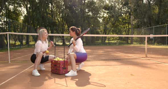 Two Young Women Sitting with Box for Tennis Balls