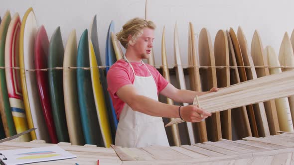 Caucasian male surfboard maker working in his studio and making a wooden surfboard