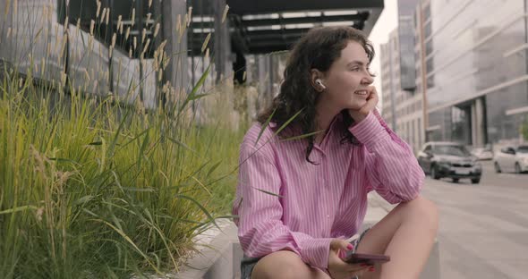 Portrait of happy woman in pink shirt using a mobile phone, typing text messages, listening music