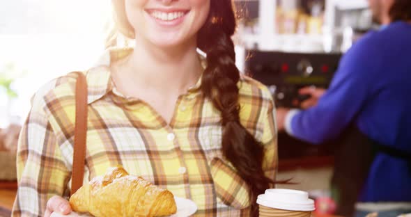 Beautiful woman holding coffee and croissant at counter