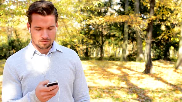 Young Man Stands in the Woods and Via Mobile Phone and Headphones Listens To Music