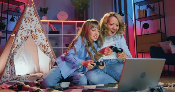 mom and her teen daughter enjoying video games on computer using joysticks