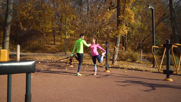 Fit couple holding each other and stretching legs on sports ground in autumn