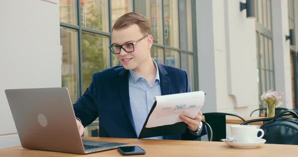 A Businessman is Looking Through Documents and Working on a Laptop