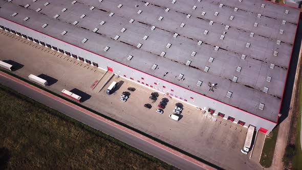 Zoom Out Aerial Shot of Industrial Warehouse/ Storage Building/ Loading Area where Many Trucks Are L
