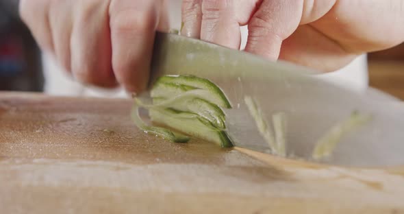 Slow motion close up of a chef knife slicing a cucumber