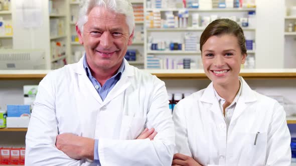 Smiling pharmacists standing with arms crossed in pharmacy