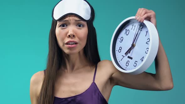 Emotional Asian Lady in Pajamas and Eyemask Showing Clock, Late for Work Closeup
