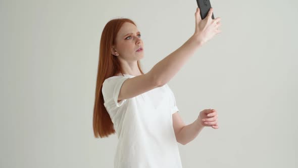 Portrait of Confused Young Woman Trying to Find Mobile Network Using Mobile Phone Standing on White