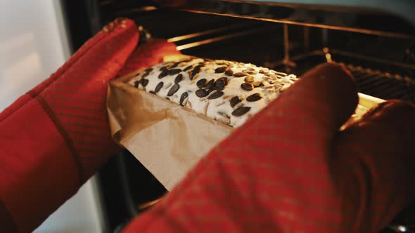 Person with Red Kitchen Gloves Putting Homemade Bread with Pumpkin Seed in the Oven. Close Up Slow