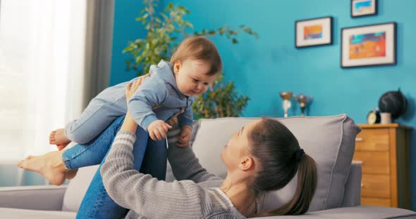 Young Energetic Mom Lies on Couch with Legs Bent Up on Which Little Son is