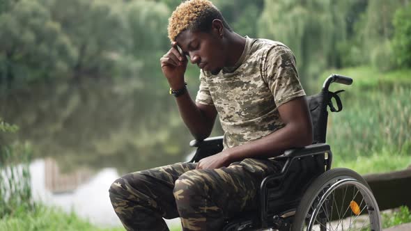 Side View Devastated African American Man in Wheelchair Thinking Sitting in Park on Lake Shore