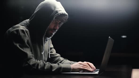 Side View of Young Bearded Programmer Hacking Online Site or Password at Desk in Dark Room