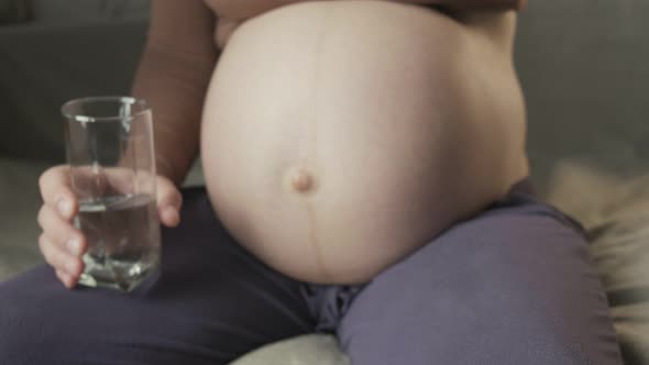 Young Pregnant Woman Sitting on Couch Taking Medicine Drinking Glass of Water