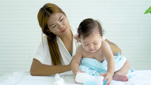 Adorable baby girl applying talcum powder on his body after bathing by his mother