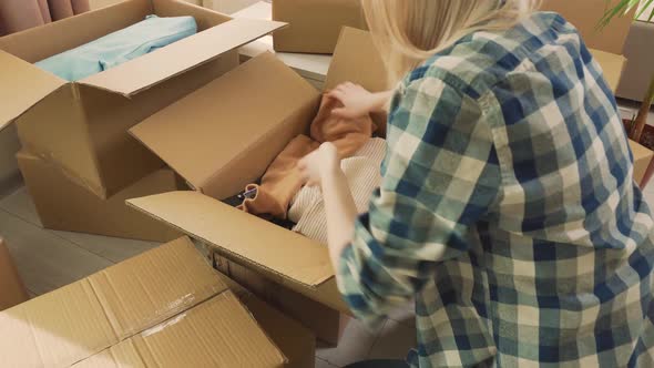 A Woman in a Plaid Shirt Puts Her Clothes in Cardboard Boxes