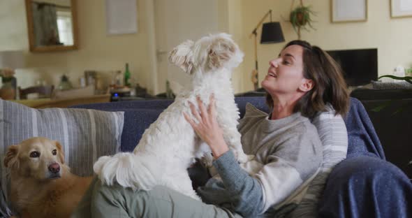 Smiling caucasian woman kissing and cuddling her pet dog sitting on sofa at home