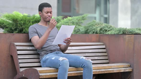 Young African Man Reading Documents in Disappointment Outdoor