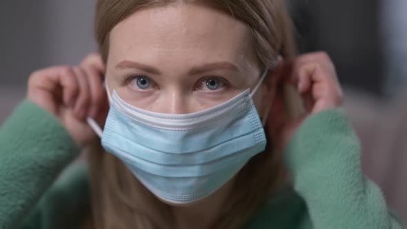 Closeup Young Woman Putting on Covid19 Face Mask Looking at Camera