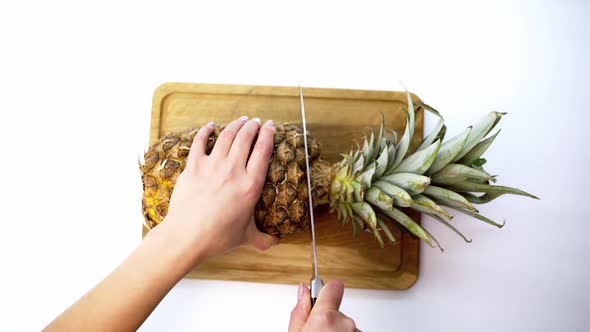 Pineapple against white background. Slicing ripe pineapple with sharp knife on table