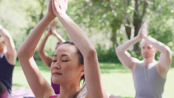 Group of diverse young people meditating and practicing yoga together at the park