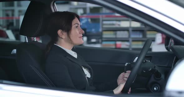 Side View of Confident Caucasian Woman Sitting on Driver's Seat in New Car, Showing Keys at Camera