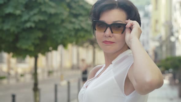 Close-up Portrait of Confident Mid-adult Caucasian Lady Putting on Sunglasses and Smiling at Camera