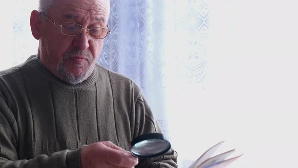 A Single Man Reads a Book with a Magnifying Glass