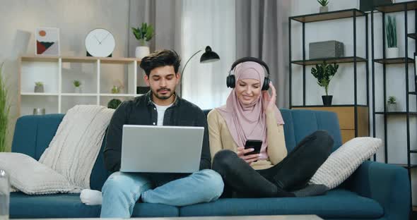 Woman in Hijab Listening Favourite Songs in Headphones Near her Concentrated Bearded Boyfriend