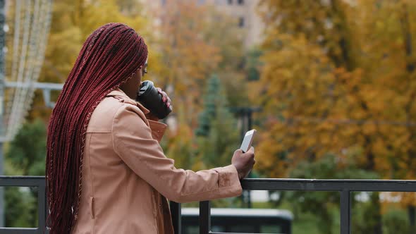 Young African American Girl Standing with Phone and Coffee on Autumn Day Outdoors