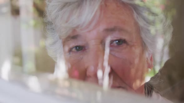 Sad senior caucasian woman looking around seen through window in slow motion