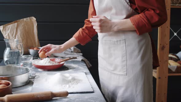 Female Baker Cracking Egg in Heap of Flour